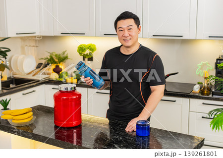 Asian young adult man shaking shaker bottle mixing healthy sports supplement drink in home kitchen 139261801