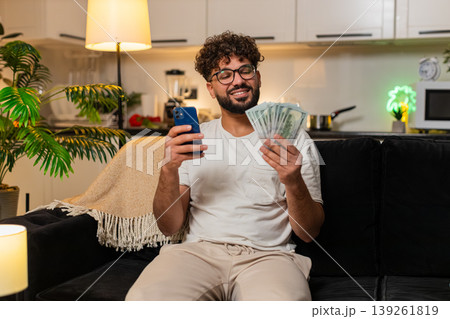 Arabian man counts dollar bills with smartphone writes salary budget numbers sets plan for expenses Arabian man counts dollar bills with smartphone writes salary budget numbers sets plan for expenses 139261819