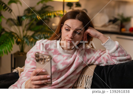 Adult woman doomscrolls smartphone news at night bored tired stressed demotivated mood sighs alone 139261838