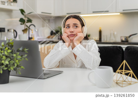 Young woman in headphones thinking with laptop leans on hands worried decision responsibility mind Young woman in headphones thinking with laptop leans on hands worried decision responsibility mind 139261850