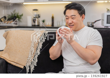 Asian man holds cup of herbal tea warms hands smiles breathes aroma enjoys pause mindful calm break Asian man holds cup of herbal tea warms hands smiles breathes aroma enjoys pause mindful calm break 139261927