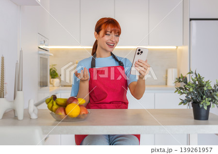 Young woman at bar counter makes video call on smartphone waves hello and shows clean tidy kitchen 139261957