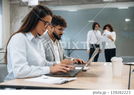 Sitting by the table with laptop. Group of people are working in the office together as a team 139262223