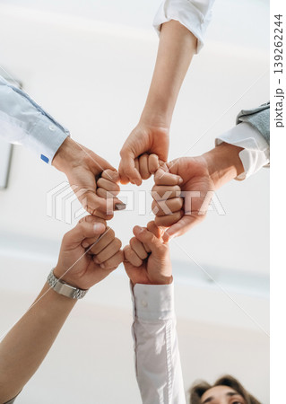 View from below of coworkers knocking fists in the office. Conception of teamwork, unity, success View from below of coworkers knocking fists in the office. Conception of teamwork, unity, success 139262244