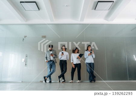 By the wall. Front view of four office workers that are standing indoors and waiting 139262293