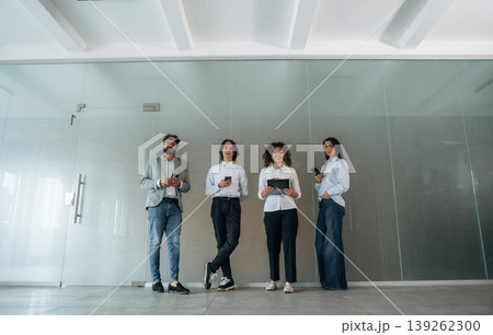 Front view of four office workers that are standing indoors and waiting Front view of four office workers that are standing indoors and waiting 139262300