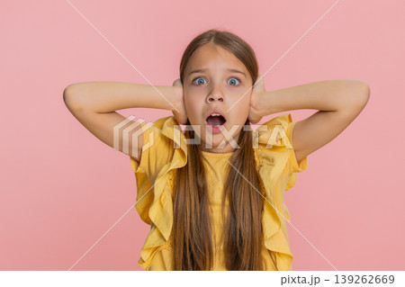 Child girl kid covers ears with hands opens eyes wide showing fear or panic from loud noise or sound 139262669