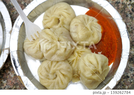 Plate of delicious steamed momos with spicy red chutney served on a disposable plate Plate of delicious steamed momos with spicy red chutney served on a disposable plate 139262784