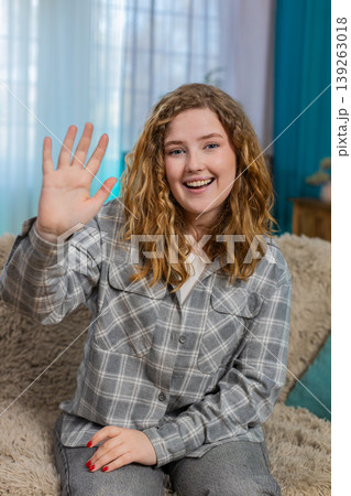 Woman sitting on sofa smiling and waving hand hello with joyful face greeting in friendly manner 139263018
