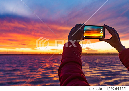 Hand photographing seascape at sunset with mobile phone 139264535
