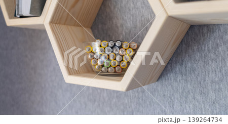 A young woman places a glass bowl filled with used batteries onto a wooden shelf for future disposal. This process demonstrates conscious household waste sorting and care for the environment. 139264734