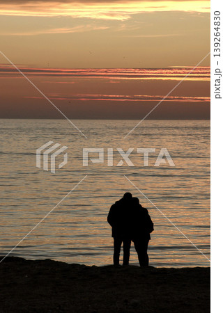 Silhouette of Couple on Beach at Sunset. A peaceful scene of a couple enjoying a golden sunset by the calm sea, captured in silhouette on a sandy shore. 139264830