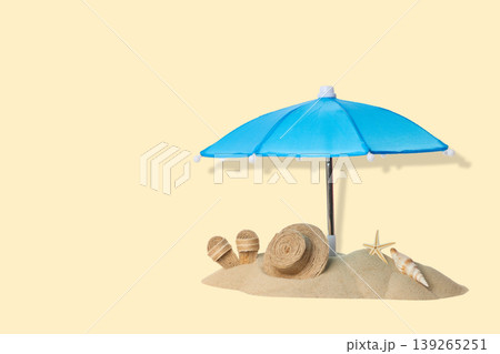 Blue umbrella stands over sand with seashells and summer items 139265251
