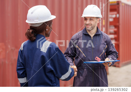Smiling mid-adult Caucasian male and Black female logistics professionals shaking hands at Asian shipping port. Smiling mid-adult Caucasian male and Black female logistics professionals shaking hands at Asian shipping port. 139265302