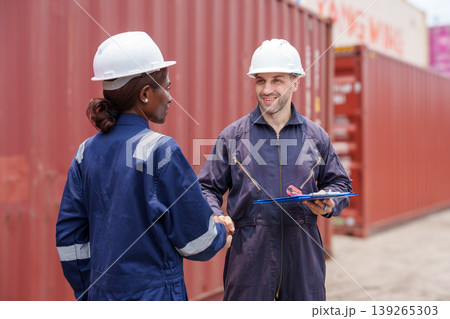 Smiling mid-adult Caucasian male and Black female logistics professionals shaking hands at Asian shipping port. Smiling mid-adult Caucasian male and Black female logistics professionals shaking hands at Asian shipping port. 139265303
