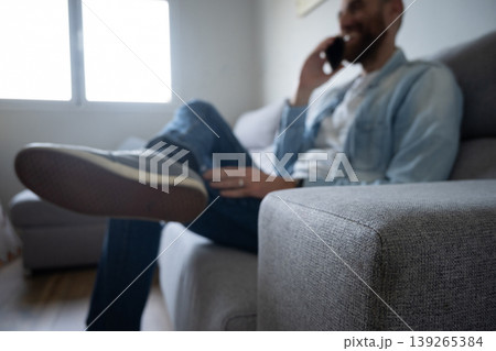 Man talking on smartphone sitting on sofa at home, relaxed lifestyle scene 139265384