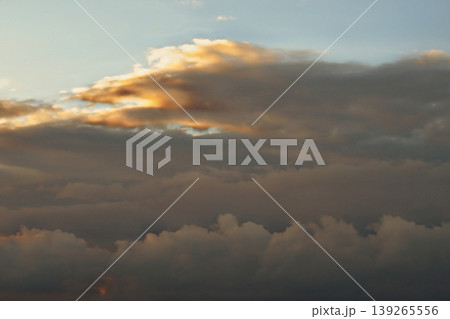 Dramatic Golden Sunset Clouds on Dark Blue Sky. Breathtaking high-contrast sky at sunset. Golden light illuminates dark storm clouds against a deep blue dusk sky. 139265556