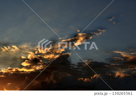 Dramatic Golden Sunset Clouds on Dark Blue Sky. Breathtaking high-contrast sky at sunset. Golden light illuminates dark storm clouds against a deep blue dusk sky. 139265561