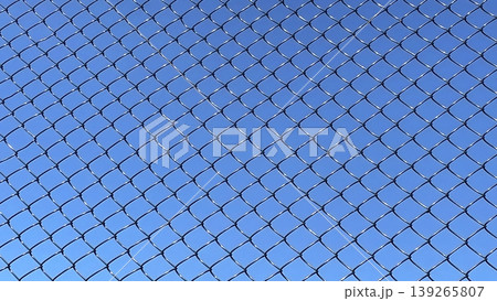 Chain Link Fence and Blue Sky. A close up, full frame shot of a shiny chain link fence against a clear, vibrant blue sky. Chain Link Fence and Blue Sky. A close up, full frame shot of a shiny chain link fence against a clear, vibrant blue sky. 139265807