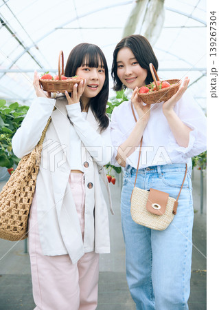 いちご狩りを楽しむ二人の若い女性・ビニールハウスで苺の入ったバスケットを持って笑顔のフレンド 139267304