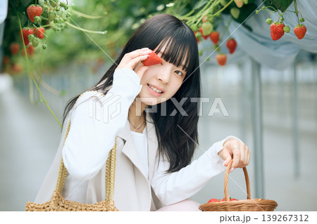 いちご狩りを楽しむ若い女性・ハウス栽培のストロベリーファームで苺を持って微笑む日本人女性 139267312