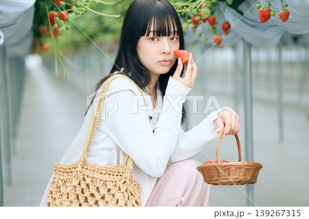 いちご狩りハウスで摘みたてのイチゴを頬に寄せる若い女性・春のレジャー体験 いちご狩りハウスで摘みたてのイチゴを頬に寄せる若い女性・春のレジャー体験 139267315