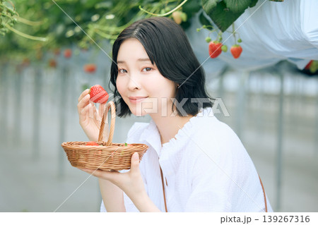 いちご狩りを楽しむ若い女性・ビニールハウスで摘みたてのイチゴを持ち微笑む日本人女性 139267316