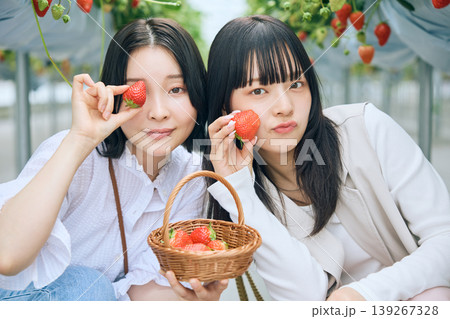 いちご狩りを楽しむ若い女性二人組・苺を持ってポーズするビニールハウスでの友達との思い出 いちご狩りを楽しむ若い女性二人組・苺を持ってポーズするビニールハウスでの友達との思い出 139267328