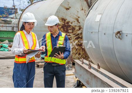 Asian male and female engineers inspecting an industrial site with large storage tanks. 139267921