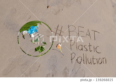 Earth shape with plastic waste texture beside handwritten message “#BEAT Plastic Pollution” on beach sand, representing global awareness of environmental pollution 139268815