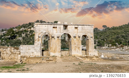 The Roman Arch of Modestus rising over excavated ruins at ancient Patara archaeological site, Lycia, Turkey. A well-preserved triumphal gate under dramatic sunset sky The Roman Arch of Modestus rising over excavated ruins at ancient Patara archaeological site, Lycia, Turkey. A well-preserved triumphal gate under dramatic sunset sky 139270833