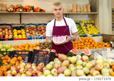 A male salesman in an apron carefully places ripe watermelons on supermarket counter A male salesman in an apron carefully places ripe watermelons on supermarket counter 139271970