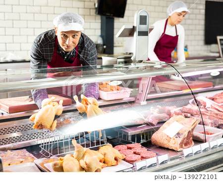 Butcher shop seller laying raw chickens in display case 139272101