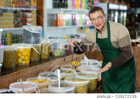 Smiling vendor inviting to buy marinated olives in grocery store Smiling vendor inviting to buy marinated olives in grocery store 139272130