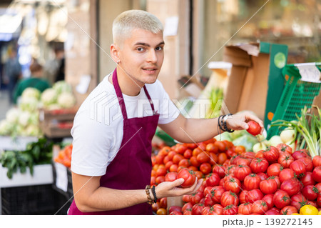 Young guy seller puts tomatoes in vegetable shop 139272145