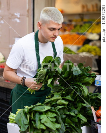 Young guy seller puts spinach in vegetable shop Young guy seller puts spinach in vegetable shop 139272295