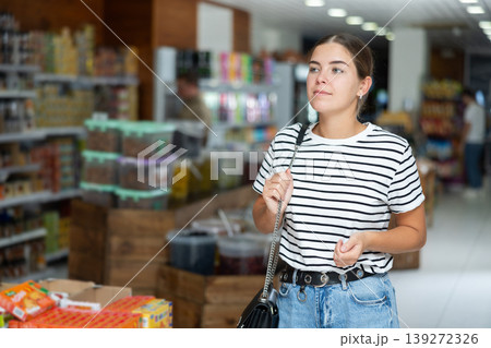 Young female shopper looking for necessary products in supermarket Young female shopper looking for necessary products in supermarket 139272326