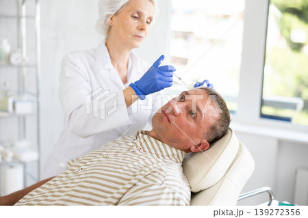 Man applying rejuvenating treatments by female doctor. Man applying rejuvenating treatments by female doctor. 139272356