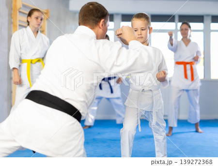 Teacher corrects boy pupil pose posture position of body, hands, legs during karate classes 139272368