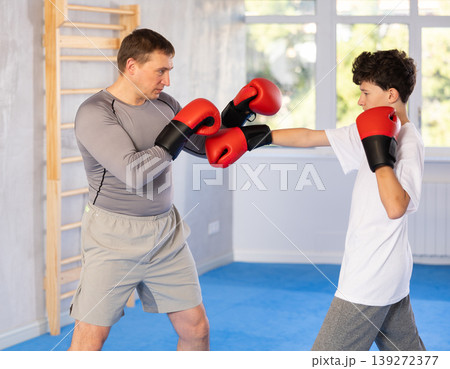Middle-aged man and teenage boy training boxing during sports classes Middle-aged man and teenage boy training boxing during sports classes 139272377