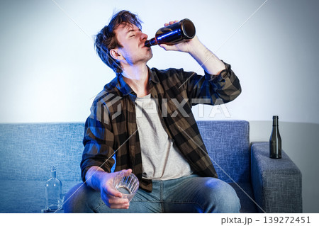 Depressed man drinking beer alone on a sofa. Concept of alcoholism, addiction, and drunkenness. Disheveled male suffering from unemployment, separation, and divorce. Depressed man drinking beer alone on a sofa. Concept of alcoholism, addiction, and drunkenness. Disheveled male suffering from unemployment, separation, and divorce. 139272451