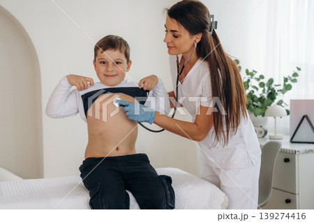 Listening to the breathing, using stethoscope. Boy is in routine appointment in clinic with female doctor Listening to the breathing, using stethoscope. Boy is in routine appointment in clinic with female doctor 139274416
