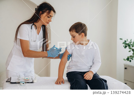 Gives an injection. Boy is in routine appointment in clinic with female doctor 139274428