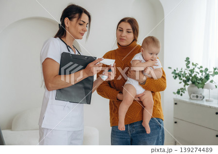 Useful medicine in hands of woman. Mother with her little baby daughter is in clinic with doctor at appointment Useful medicine in hands of woman. Mother with her little baby daughter is in clinic with doctor at appointment 139274489