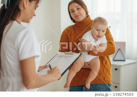 Notepad is in hands. Mother with her little baby daughter is in clinic with doctor at appointment Notepad is in hands. Mother with her little baby daughter is in clinic with doctor at appointment 139274503