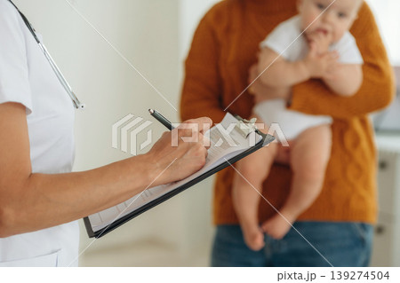 Notepad is in hands. Mother with her little baby daughter is in clinic with doctor at appointment Notepad is in hands. Mother with her little baby daughter is in clinic with doctor at appointment 139274504