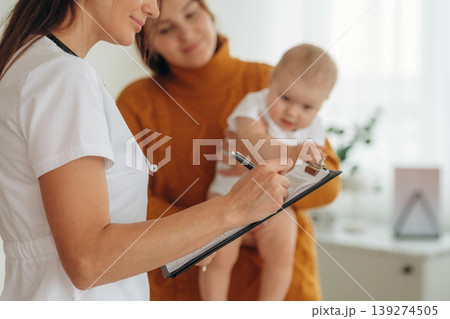 Using pen, writing information. Mother with her little baby daughter is in clinic with doctor at appointment Using pen, writing information. Mother with her little baby daughter is in clinic with doctor at appointment 139274505