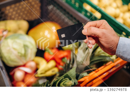 Black colored credit or debit card in hand. Close up view of man that is in the grocery store Black colored credit or debit card in hand. Close up view of man that is in the grocery store 139274978