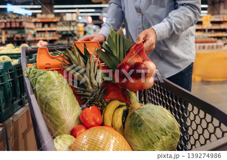 Cabbage, tomatoes, bananas in the shopping cart. Close up view of man that is in the grocery store Cabbage, tomatoes, bananas in the shopping cart. Close up view of man that is in the grocery store 139274986