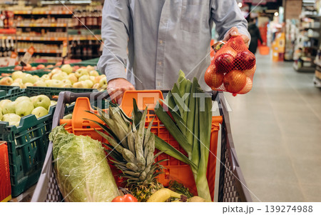Cabbage, tomatoes, bananas in the shopping cart. Close up view of man that is in the grocery store Cabbage, tomatoes, bananas in the shopping cart. Close up view of man that is in the grocery store 139274988